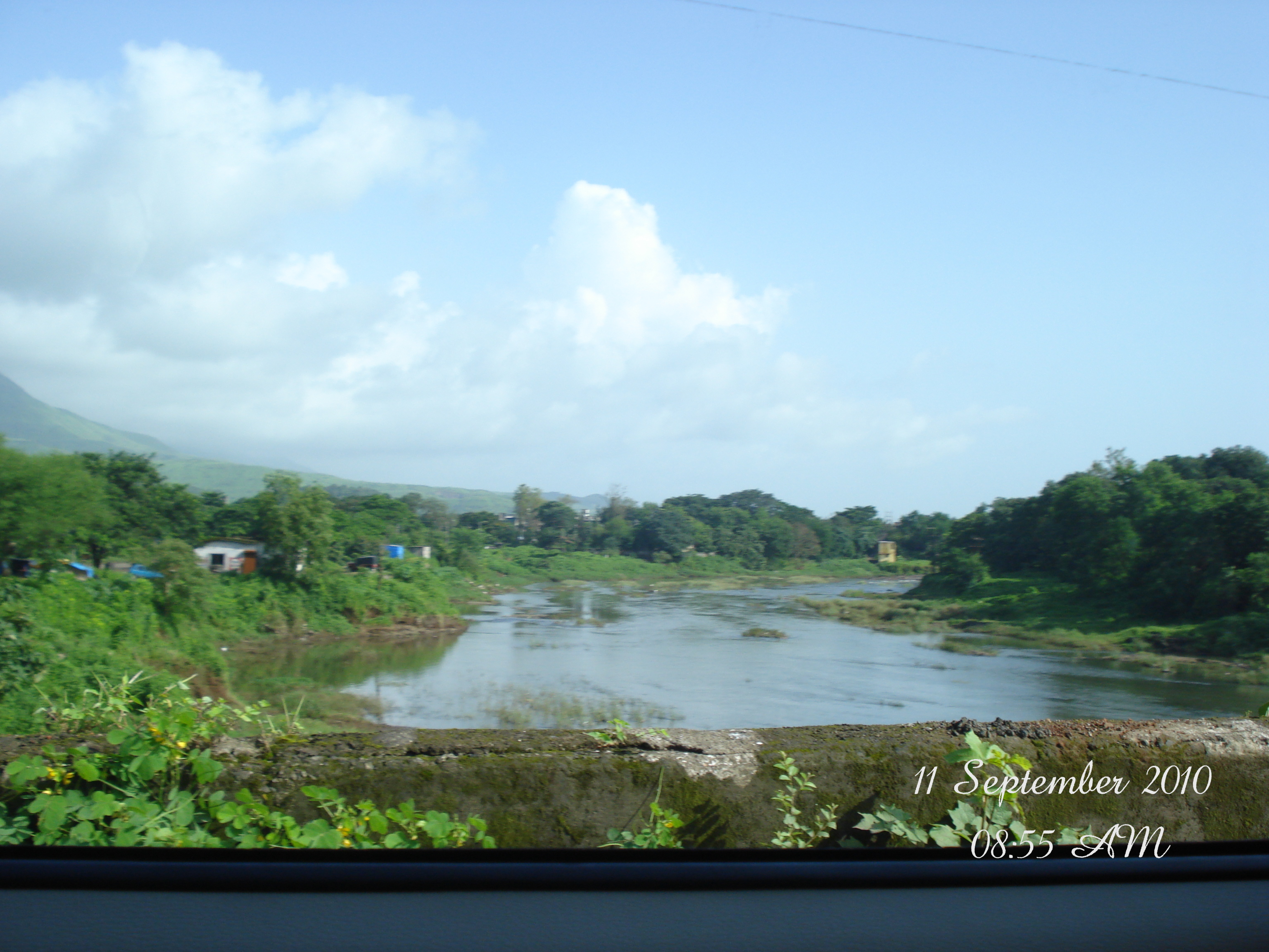 River bordered by green trees and hills in Karjat
